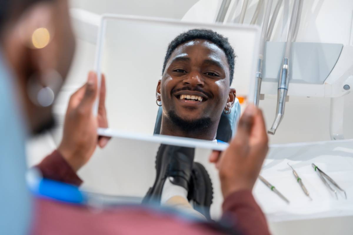 Young man checks his teeth in the mirror at the dental clinic, happy with the results of the treatment