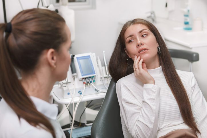 Young woman having toothache, visiting dentist.